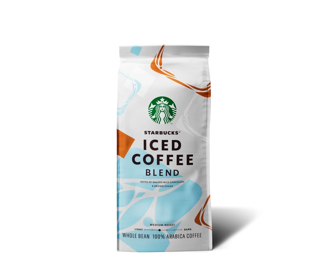 Bílé balení zrnkové kávy Starbucks® Iced Coffee Blend stojí samostatně na světlém, neutrálním pozadí. Uprostřed obalu je zelené logo Starbucks se sirénou a pod ním výrazný nápis „ICED COFFEE BLEND“. Obal je doplněn světle modrými a oranžovými grafickými prvky. Ve spodní části je uvedeno, že jde o středně praženou kávu z 100 % arabiky, s chuťovými tóny sladové mléčné čokolády a hnědého cukru. Obal vrhá jemný stín doprava, pozadí neobsahuje žádné další objekty.
