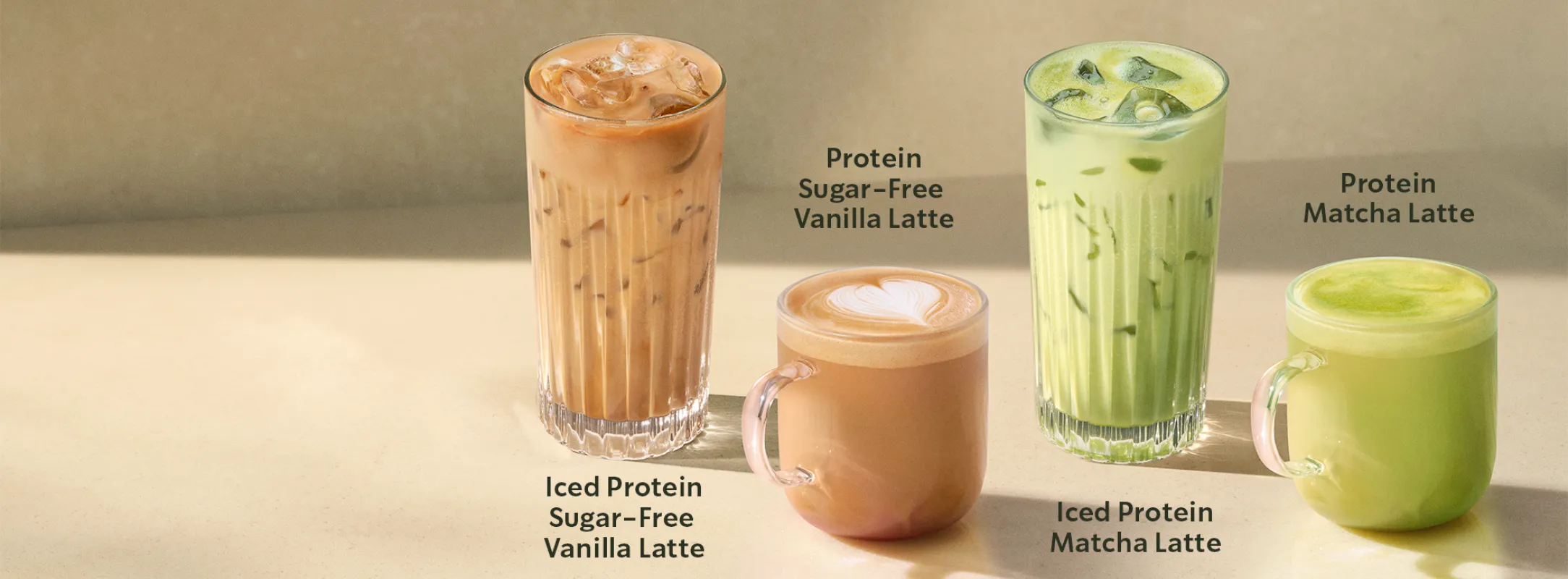 Čtyři nápoje na světlém pozadí: dva kávové Protein Sugar‑Free Vanilla Latte (jeden ledový, jeden teplý) a dva matcha nápoje Protein Matcha Latte (jeden ledový, jeden teplý)