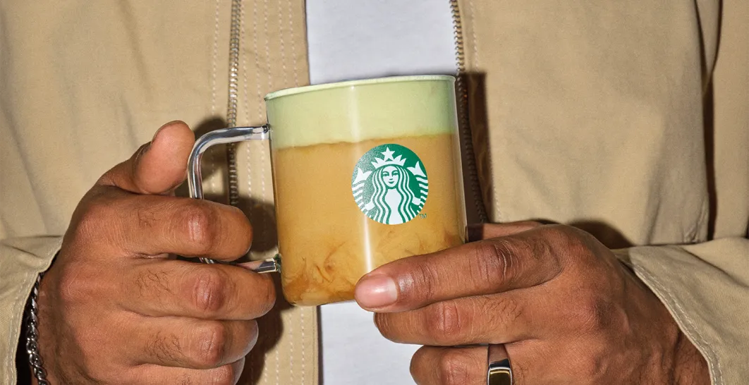 šlověk drží před sebou nápoj v hrnečku starbucks