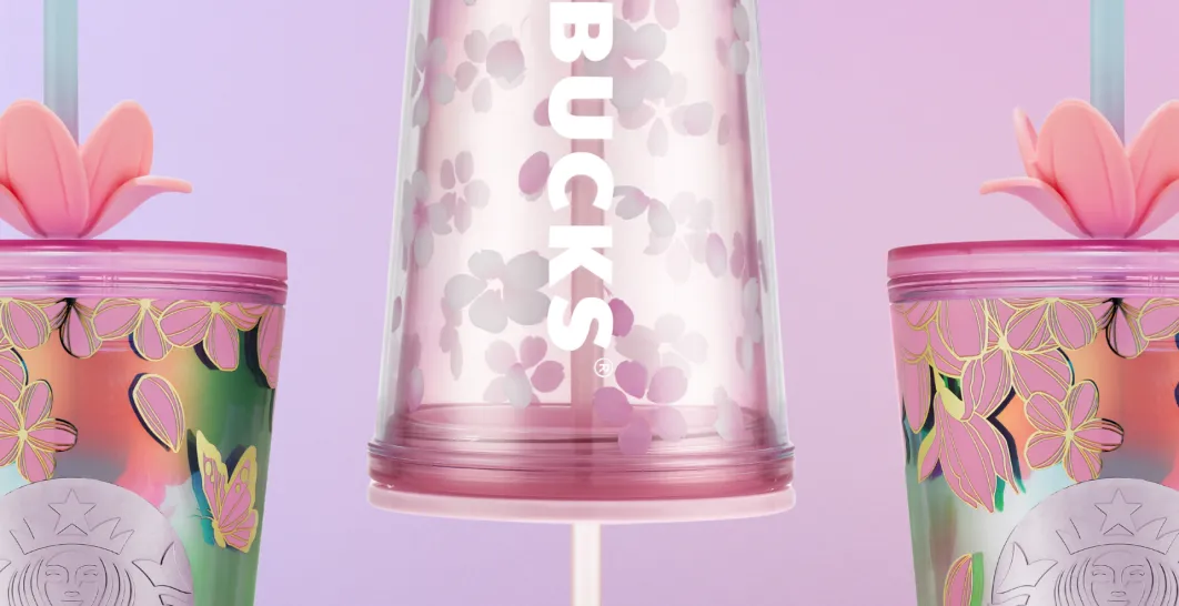 Detailní záběr na tři plastové tumblery Starbucks s brčkem v jemných růžových a pastelových tónech. Kelímky jsou zdobené květinovými motivy inspirovanými jarem, s kombinací růžové, zelené a zlatých linií. Uprostřed je průhledný tumbler s bílým svislým nápisem Starbucks a drobným květinovým vzorem, po stranách jsou barevnější kelímky s výraznějším květinovým dekorem a plastickým víčkem. Pozadí je jednolité, světle fialové, které zvýrazňuje jarní a lehký charakter produktů.
